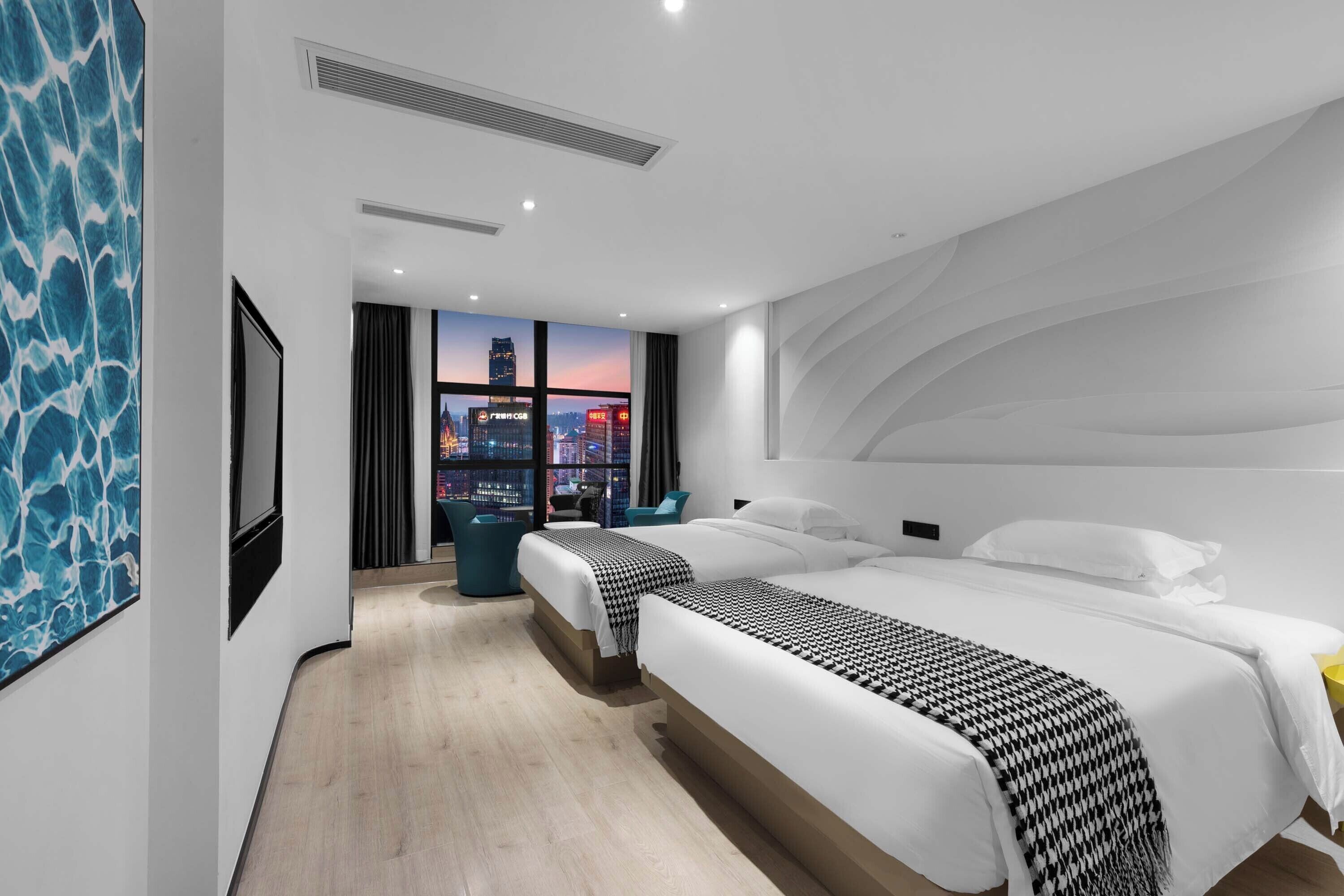 Habitación de hotel moderna con una cama grande, vistas a un paisaje urbano y un cuadro abstracto azul en la pared.