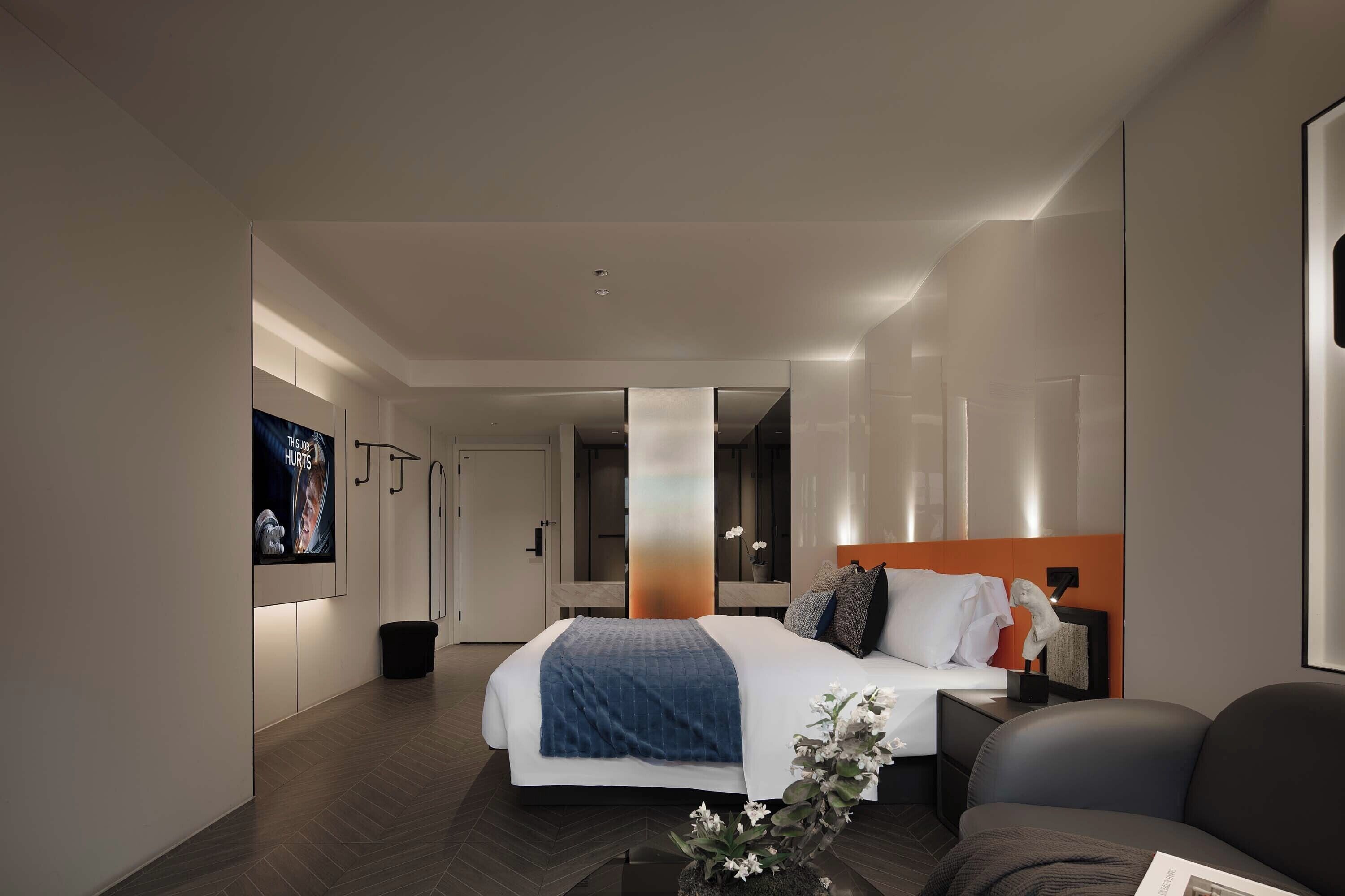 Una habitación de hotel moderna con una cama grande, un área de descanso y un baño visible a través de una pared de vidrio.