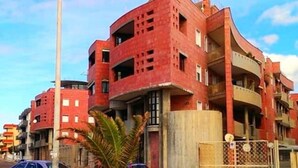 Un immeuble résidentiel à plusieurs étages, doté de balcons et d’une entrée sécurisée par un portail.