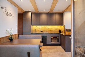 Eine moderne Küche mit Holzbalken, grauen Schränken, einer Holzrückwand und einem Essbereich mit einer Bank und einem Topf mit Pflanze.