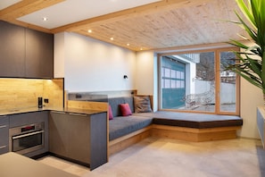 A modern kitchen with built-in appliances, a wooden bench with cushions, and a large window offering a view. - Apartment "Wildschön" with Mountain Views, Shared Garden and Wi-Fi (Grafenweg)