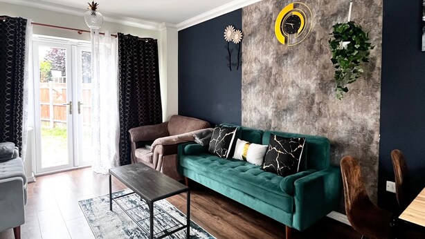 A modern living room with a teal sofa, a wooden coffee table, and a patterned rug. - Canterbury Charm - Spacious 4 Bedroom House (Canterbury)