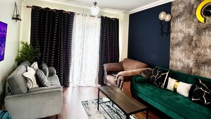 A living room with a grey sofa, a green sofa, a coffee table, and a patterned curtain. - Canterbury Charm - Spacious 4 Bedroom House (Canterbury)