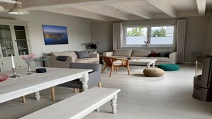 A spacious living room with a white sofa, a dining table with benches, and a large window with curtains. - Seenixe by Interhome (Altwarp)