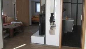 Un soggiorno moderno con divano, tavolino e televisore. Si apre una porta che dà accesso a un bagno con doccia e servizi igienici.