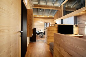 A wooden interior with a dining area, a TV on a wooden stand, and a ceiling with exposed beams.