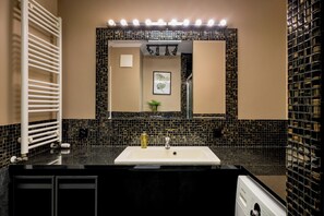 A modern bathroom with a black and beige tiled backsplash, a white sink, and a large mirror. - RentPlanet - Jedności Narodowej (Wrocław)