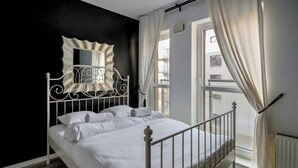 A neatly made bed in a room with a black accent wall, a window with curtains, and a radiator. - RentPlanet - Jedności Narodowej (Wrocław)