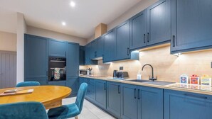 A modern kitchen with blue cabinets, a wooden dining table, and a built-in oven.