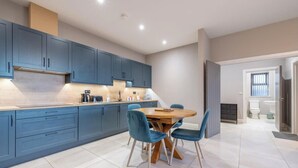 A modern kitchen with blue cabinets, a dining table with chairs, and a visible bathroom with a toilet and sink.