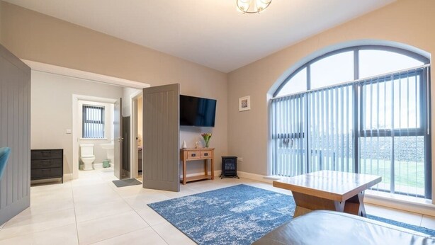 A spacious room with a large window, a flat-screen TV, a wooden table, and a blue rug.