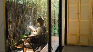 A person sitting on a chair by a window with bamboo plants, reading a book. - Family Home Villa Nearby Ba Na Hills (Đà Nẵng)