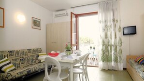 Ein Wohnzimmer mit einer Couch, Esstisch, Stühlen, einem Fernseher und einem Fenster mit Vorhängen.