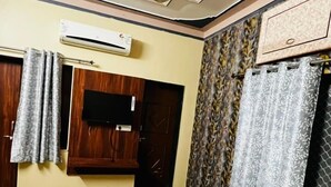 Quarto de hotel com cama, ventilador de teto, ar condicionado, televisão e cortinas estampadas.