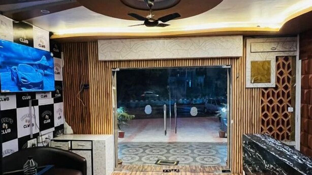 Interior moderno com piso de madeira, ventilador de teto e uma TV exibindo um carro.
