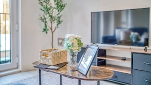 Un soggiorno moderno con una TV a schermo piatto, un tavolino in legno, un vaso con fiori, un cesto in vimini e una foto incorniciata.