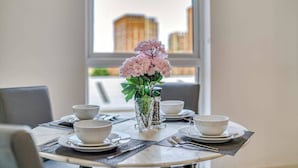Tavola imbandita per quattro persone, con un vaso di fiori rosa al centro, una finestra che si affaccia su un panorama urbano e un arredamento moderno.