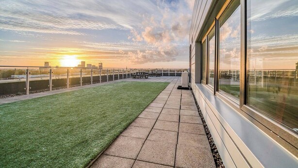 Una terrazza sul tetto con vista sul tramonto sullo skyline cittadino, con una zona verde e un percorso pedonale lastricato.