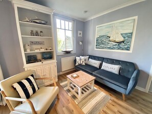 A living room with a blue sofa, a striped chair, a small wooden table, and a bookshelf with decorative items. - Ostseestrand-14, ideal location on the beach, 2 balconies with ocean views, elevator, sauna (Kühlungsborn)