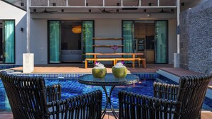 Uma área moderna de piscina ao ar livre, com duas cadeiras de vime, uma mesa redonda e dois vasos decorativos.