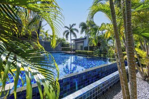 A swimming pool with blue mosaic tiles, surrounded by palm trees and a modern building in the background. - Aroha Villa Private Pool Nai Harn Beach (Rawai)
