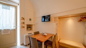 Ein Zimmer mit Holztisch, Korbstühlen, einer Bank, einem an der Wand montierten Fernseher und einer Tür mit einem Schild.