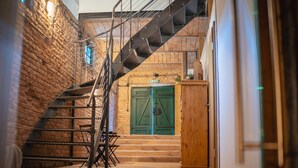 Un escalier menant à une porte en bois avec un volet vert, un mur de briques et une rambarde en métal.