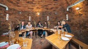 Un espace repas aux murs de briques, doté de tables et de chaises en bois, ainsi que de verres à vin et de couverts.