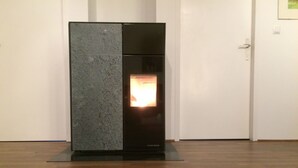 A modern fireplace with a stone facade and a glass door, set in a room with wooden flooring and white walls. - mit Garten, Grill und Terrasse by Interhome (Hagenbrunn)