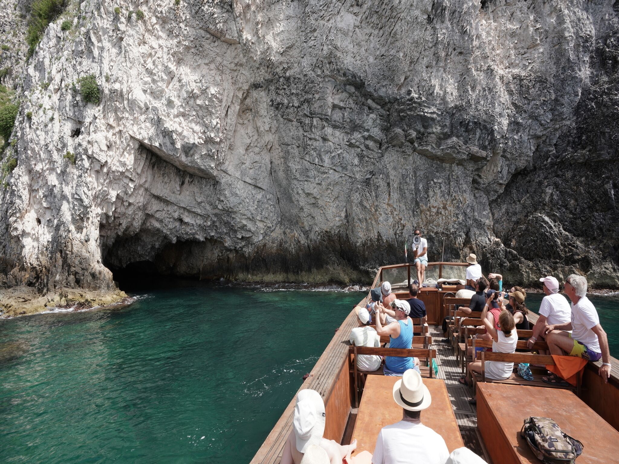 A boat with passengers, rocky cliffs, and clear water.