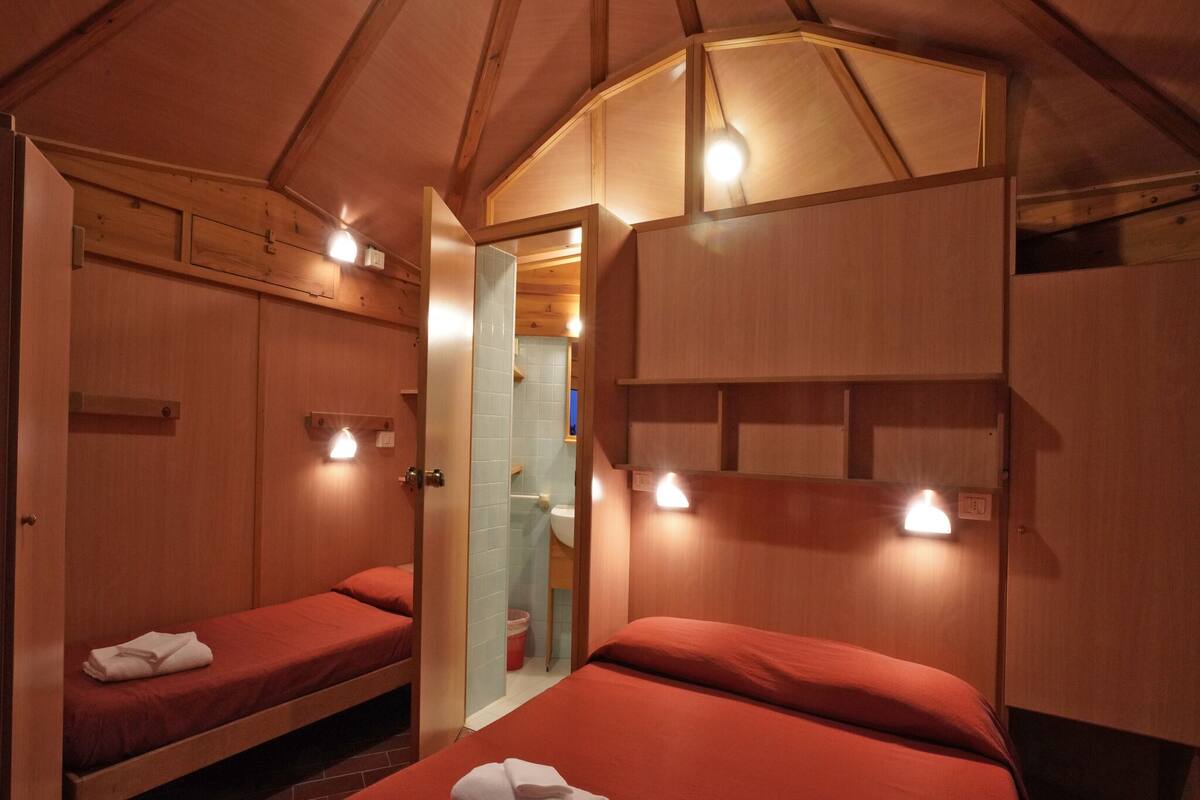 Una habitación con dos camas, paredes de madera y un tragaluz.