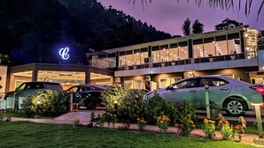 A hotel with a prominent illuminated logo, multiple cars parked in front, and a well-lit entrance.