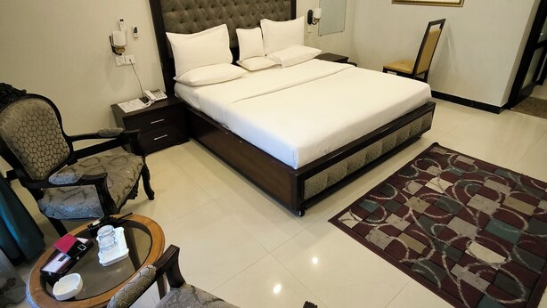 A neatly arranged hotel room with a large bed, a chair, a small table with a glass, and a clock on the wall.