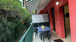 Een balkon met een tafel en stoelen, een gestreept zonnescherm en een rode muur.