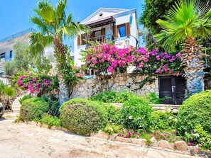 A two-story building with a stone wall, pink bougainvillea, and palm trees. - mit Blick auf das Wasser by Interhome (Kalkan)
