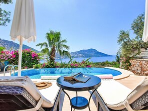 A poolside area with lounge chairs, a table, and a view of the sea and mountains. - mit Blick auf das Wasser by Interhome (Kalkan)