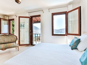 A bedroom with a large bed, a sofa, a balcony with a table and chairs, and a view of a mountainous landscape. - mit Blick auf das Wasser by Interhome (Kalkan)