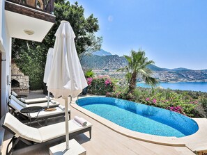 A swimming pool with lounge chairs and an umbrella, surrounded by greenery and a view of the sea and mountains. - mit Blick auf das Wasser by Interhome (Kalkan)
