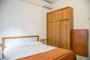 A bedroom with a bed, wooden wardrobe, and an air conditioning unit. - Comfy accommodation with balcony (Eraclea Mare)