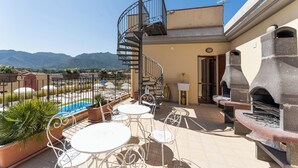 Terrassa al terrat amb seients exteriors, una escala caragolada, una graella de pedra i vistes a les muntanyes.
