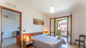 Un dormitori amb llit, abacines, un quadre i vista a un balcó amb un edifici.