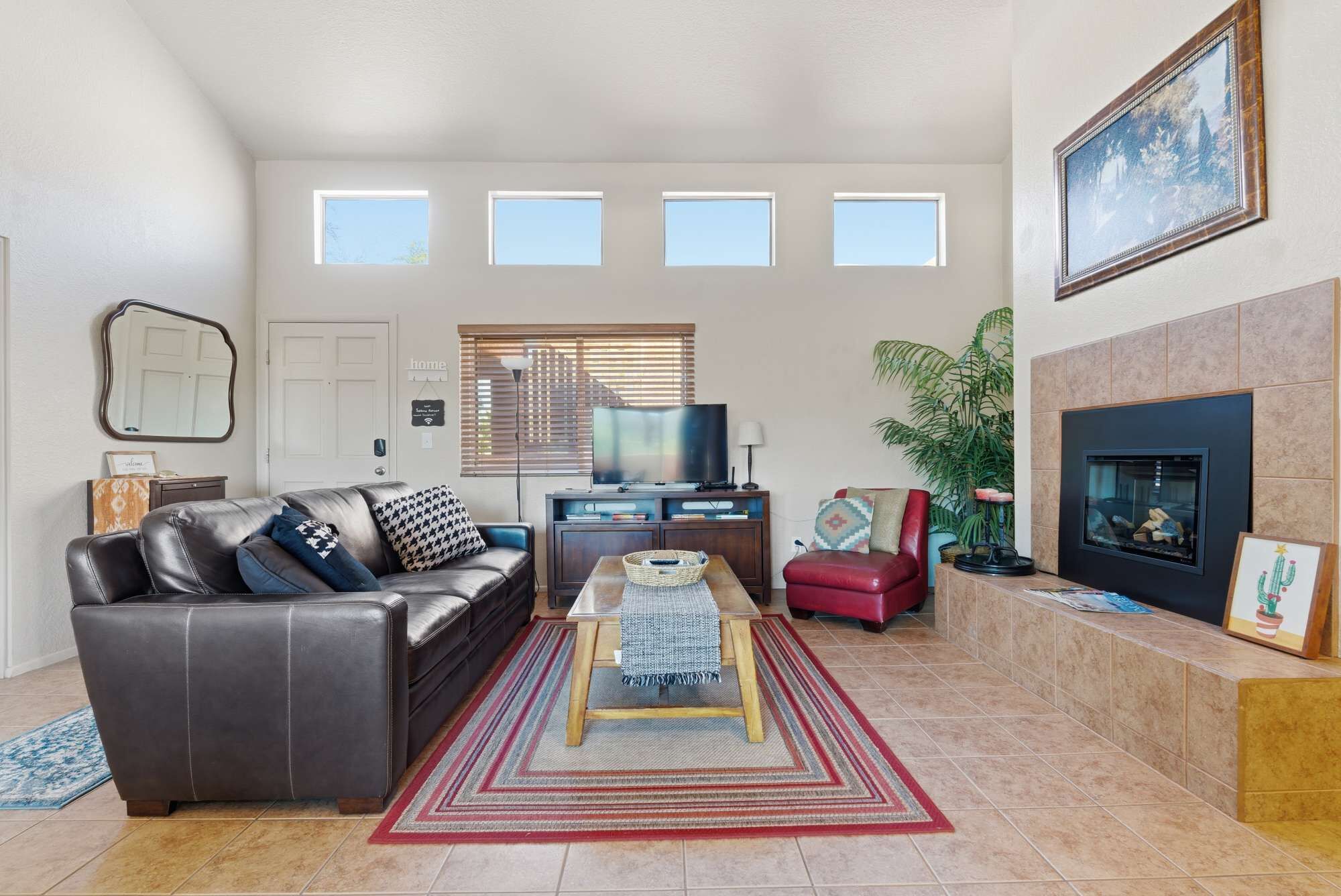 Ein Wohnzimmer mit einer Ledersofa, einem Couchtisch, einem Fernseher, einem Kamin und einem großen Fenster mit Jalousien.