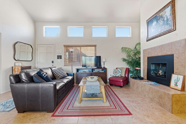 Ein Wohnzimmer mit einer Ledersofa, einem Couchtisch, einem Fernseher, einem Kamin und einem großen Fenster mit Jalousien.