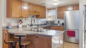 Una cocina con armarios de madera, un refrigerador de acero inoxidable, un microondas y una tetera en la isla.