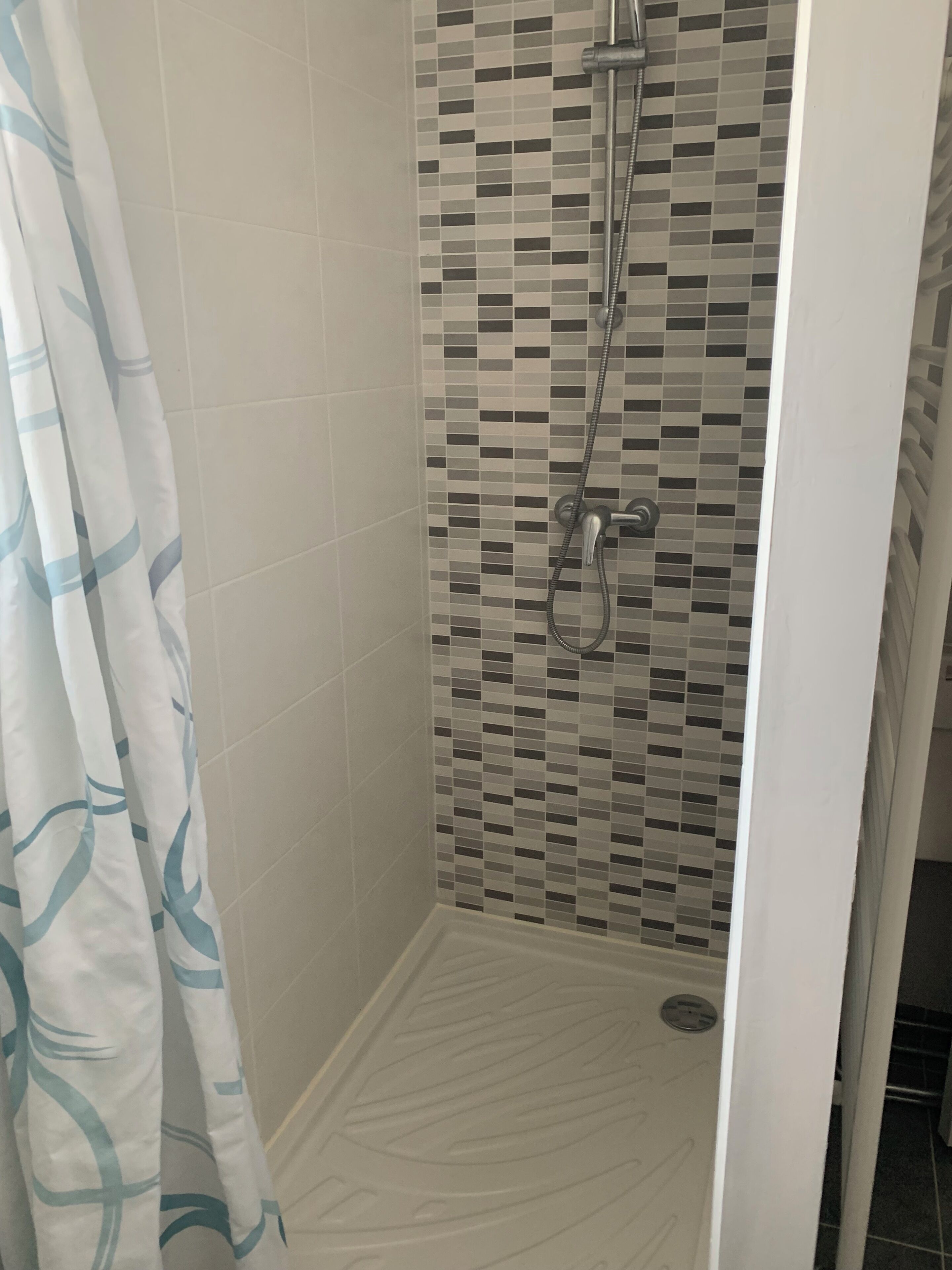 Un espace douche avec un mur carrelé et un pommeau de douche.