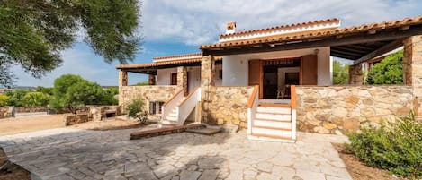 A stone building with a tiled roof, a staircase leading to the entrance, and a paved patio area.