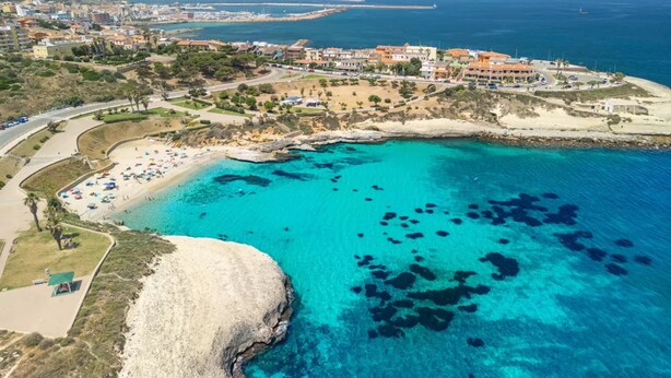 Vista aérea de una zona costera con playa, aguas azules cristalinas y una área residencial con edificios.