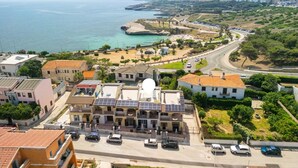 Un pueblo costero con edificios residenciales, una carretera que serpentea a lo largo de la costa y una vista despejada del mar.