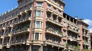 Ein mehrstöckiges Wohngebäude mit Balkonen, einer steinernen Fassade und blauem Himmel.