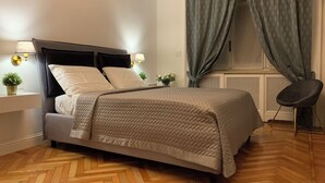 Ein ordentlich eingerichtetes Schlafzimmer mit einem Bett, Nachttischlampen, einer Topfpflanze und einem Sessel.